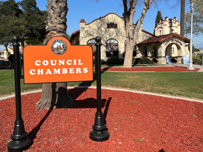 A photo of Perris City Hall in the background with a sign that says Council Chambers in the foreground.