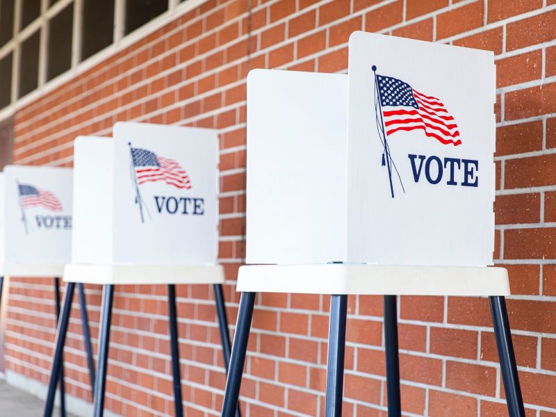 A photo of three ballot stations against a red brick wall.