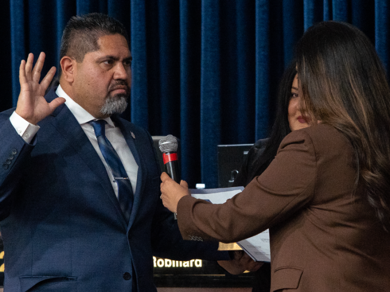 Luis Hernandez stands with one hand up in the air while taking his oath of office.