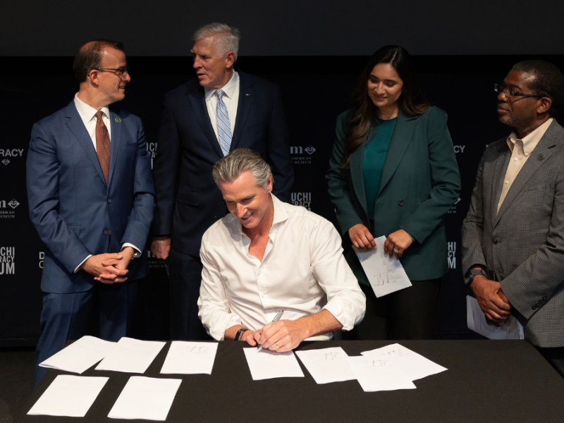 Gov. Gavin Newsom signing more than a dozen new laws regarding elections flanked by their authors.