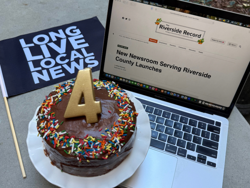A laptop open to The Record's first story, a chocolate cake with a 4 candle on it and a flag that says long live local news.