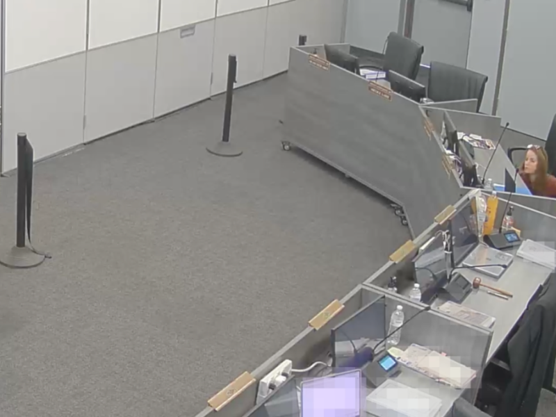 A screenshot from a surveillance video showing Melinda Anderson checking the placement of a device under a table.