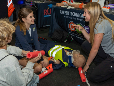 Two students listen as an educator talks about training on a healthcare mannequin.